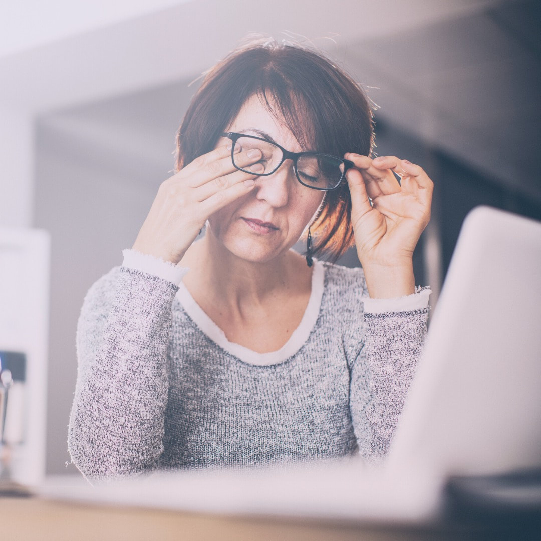 Woman rubbing her eyes and removing her glasses at a desk with laptop—a moment of pause to distract, relax, and cope.