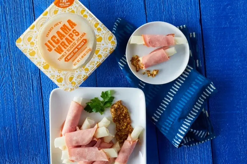Package of jicama wraps next to deli‑meat‑wrapped jicama slices on a blue background